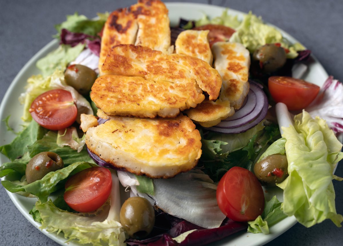 Golden brown halloumi cheese slices with olives, red onions, and tomatoes