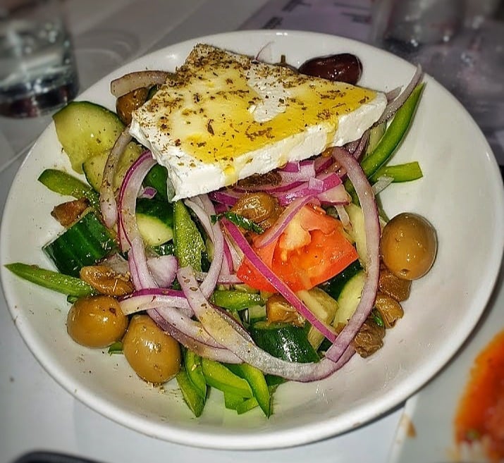 Gourmet salad with creamy goat cheese, fresh vegetables, red onion, cucumbers, and olives on white plate